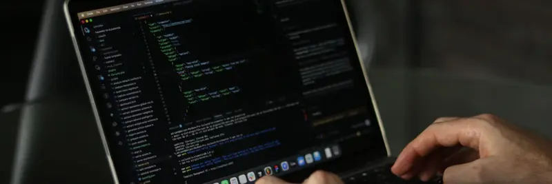 A developer typing at a laptop whose screen is filled with source code