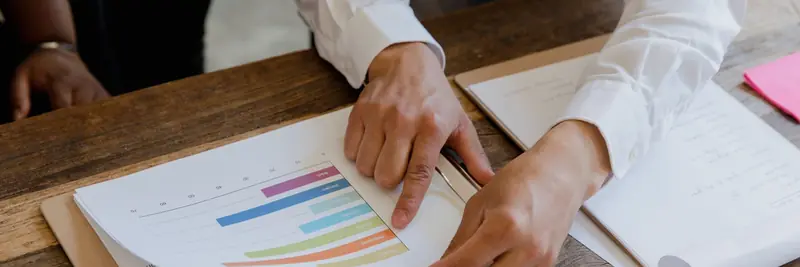 Printed data tables and a laptop spreadsheet spread across a desk
